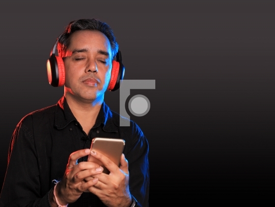 Indian Man listening to music on wireless headphones with a mobi