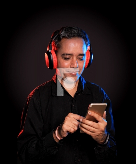 Indian Man listening to music on wireless headphones with a mobi