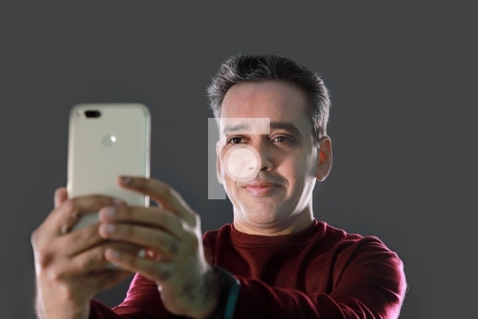 Indian Man taking a selfie with mobile phone on grey background