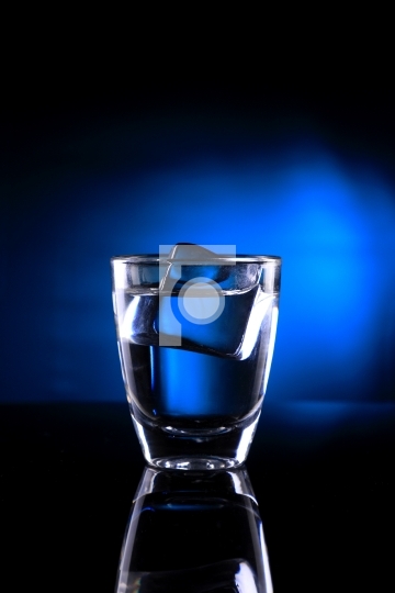 Shot Glass with an Ice Cube on Blue background